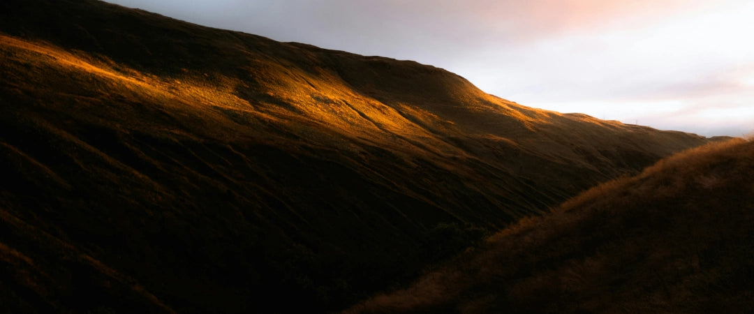 A picturesque mountain silhouette against a vibrant sunset sky filled with warm hues of orange and pink.