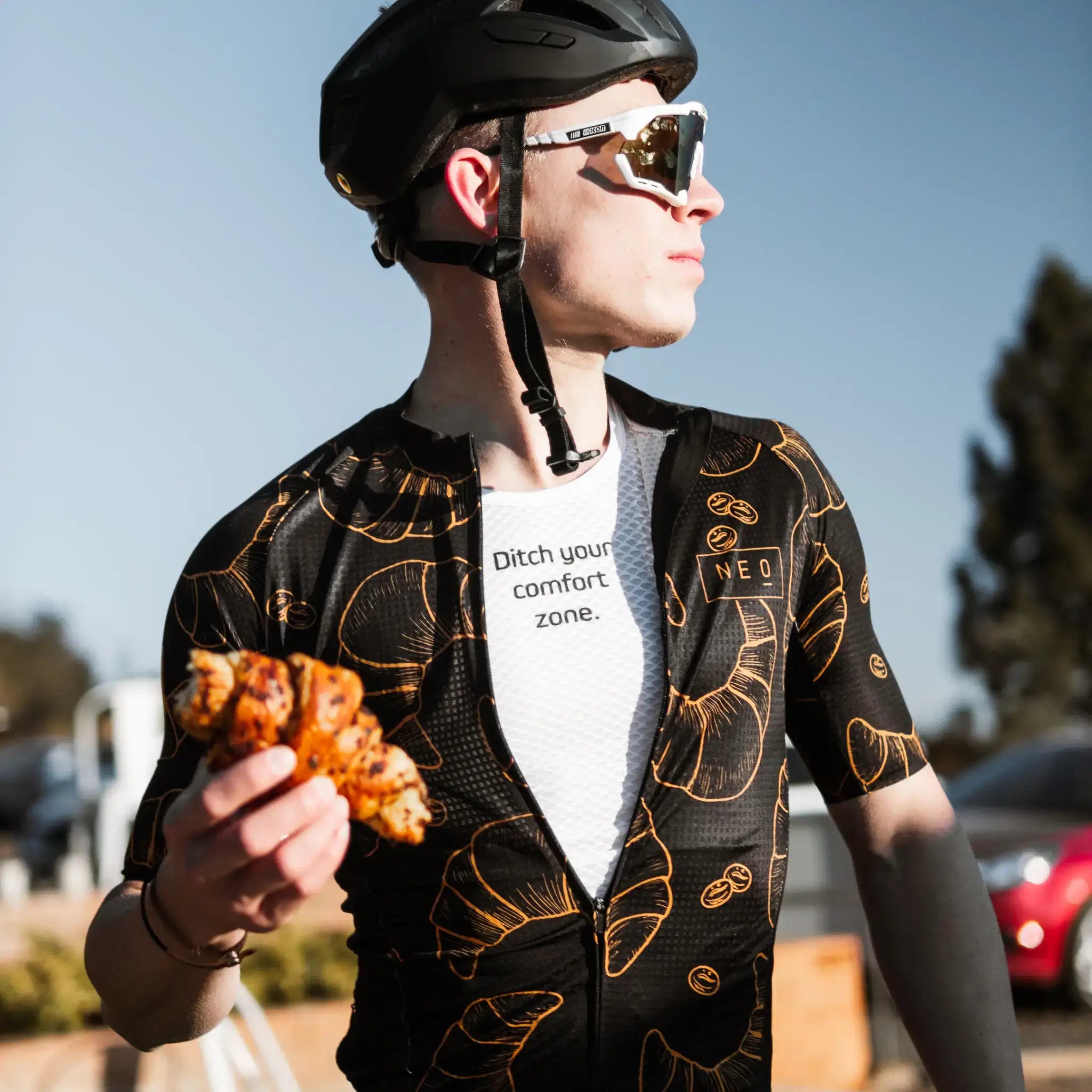Male cyclist wearing a Neo Hyphen Le Croissant jersey and a white Ditch Your Comfort Zone Baselayer Underneath