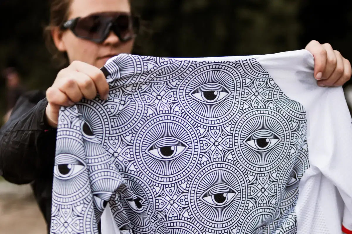 Female cyclist holding up a Neo Hyphen All-Seeing Eye cycling jersey in front of her.