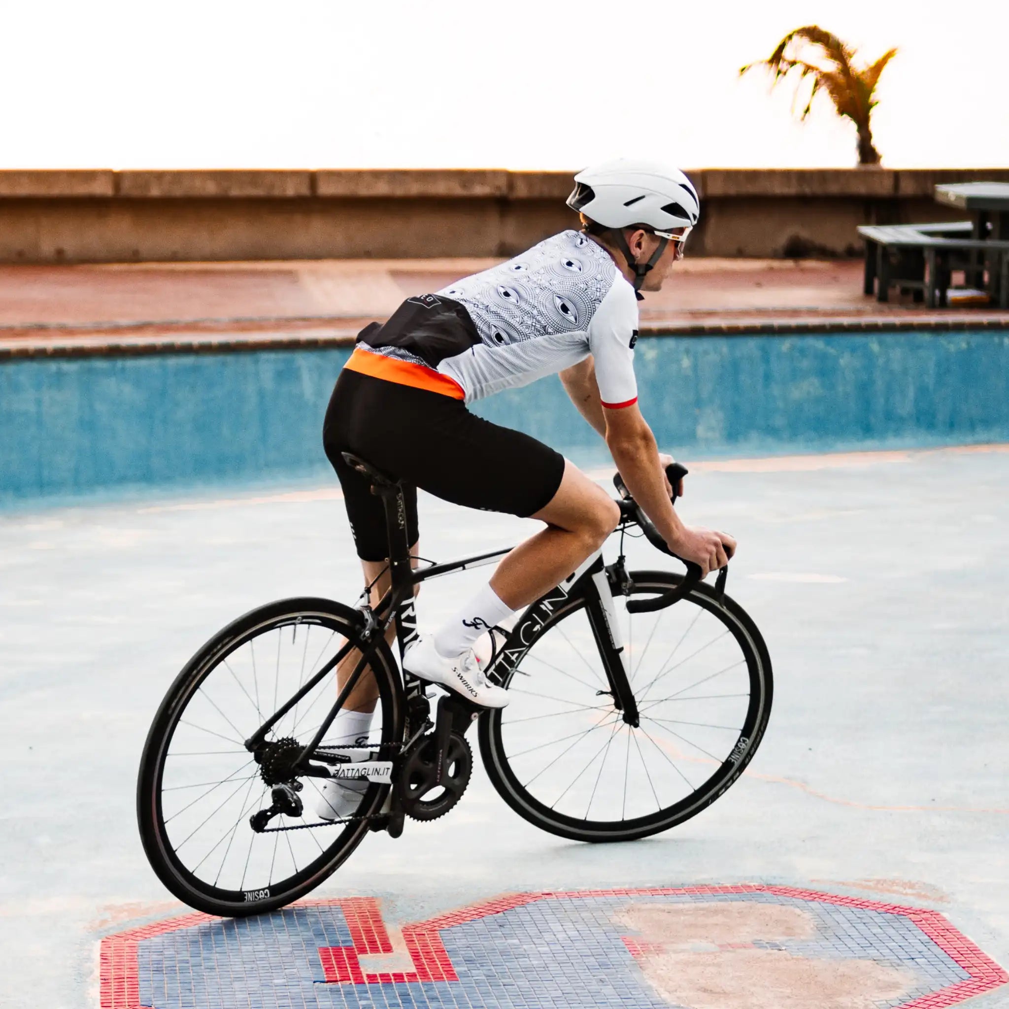 A man in a Neo Hyphen All-Seeing Eye Jersey rides a bicycle across the surface of an empty pool.