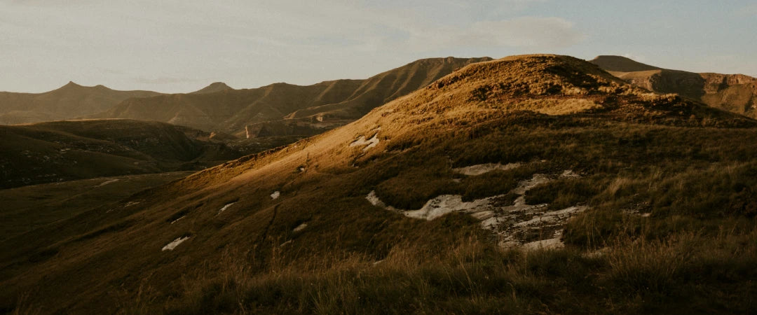 A scenic mountain with lush grass and a gentle hill in the foreground under a clear blue sky.