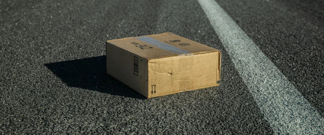 A cardboard box rests on the side of an empty road, surrounded by a quiet, desolate landscape.