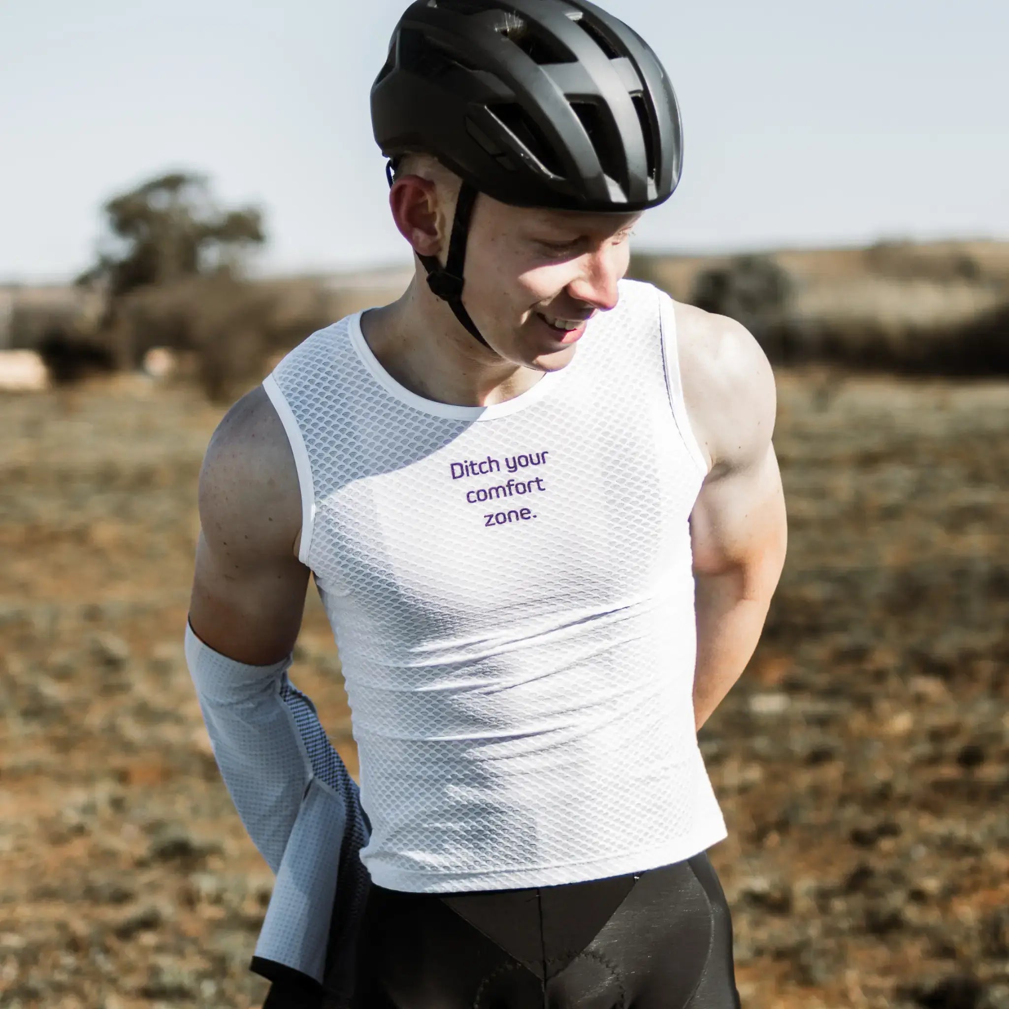A man in a white Neo Hyphen Baselayer and bike helmet stands confidently, ready for an outdoor cycle.