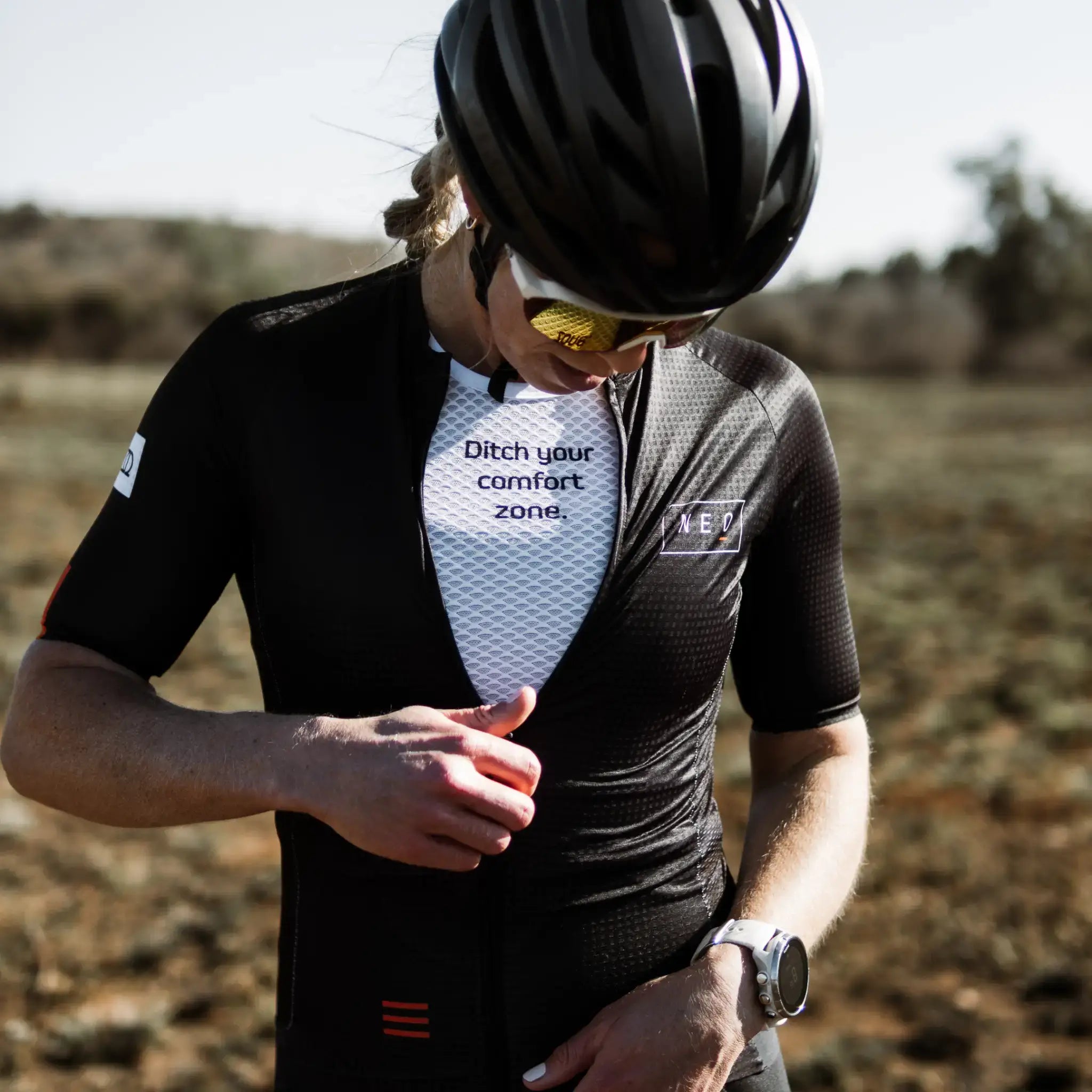Female cyclist wearing a Neo Hyphen Phantom Jersey and a white Ditch Your Comfort Zone Baselayer underneath.