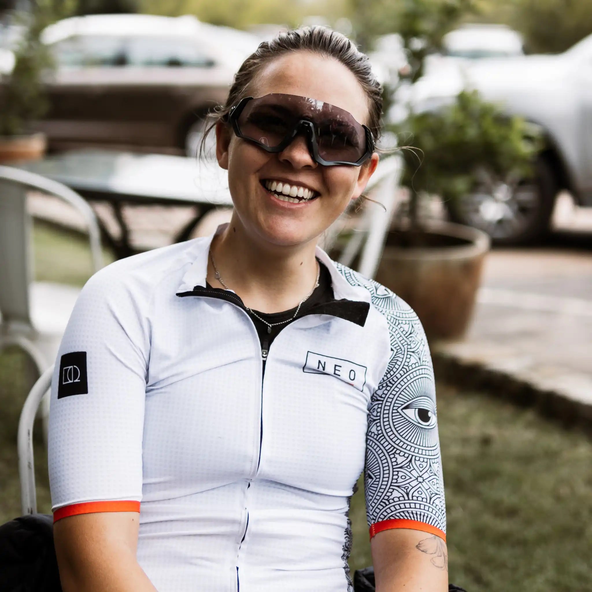 A woman with cycling sunglasses, proudly sporting a women's 'All-Seeing Eye' cycling jersey, ready to ride.