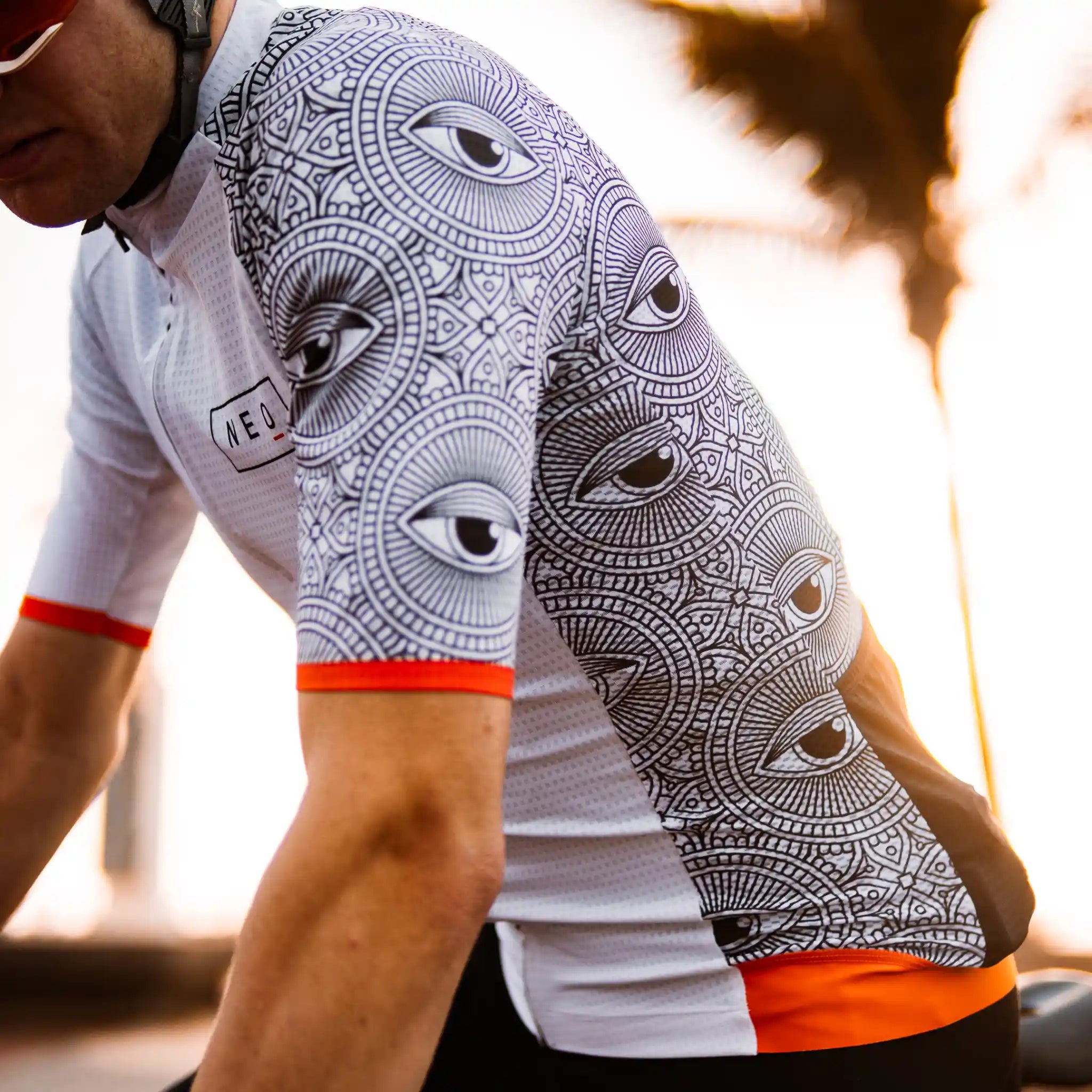 A man models the Neo Hyphen All-Seeing Eye Jersey featuring a unique eye pattern on a vibrant bicycle jersey.
