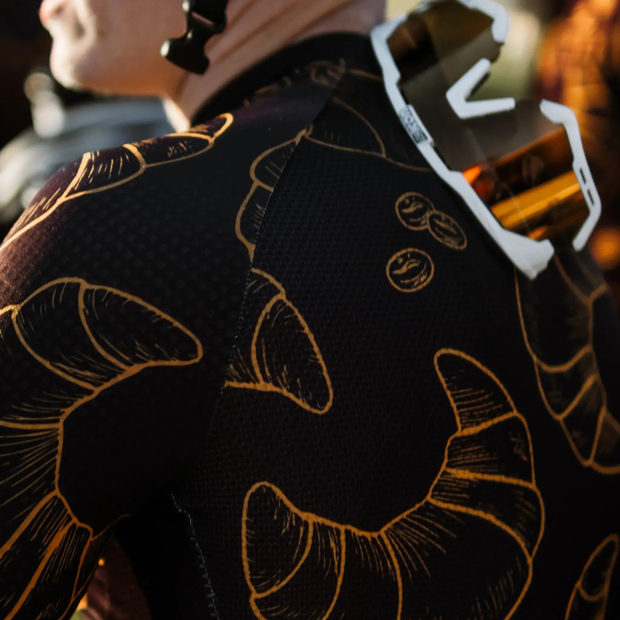 A man models a Neo Hyphen Le Croissant jersey, showcasing an eye-catching gold and black design.