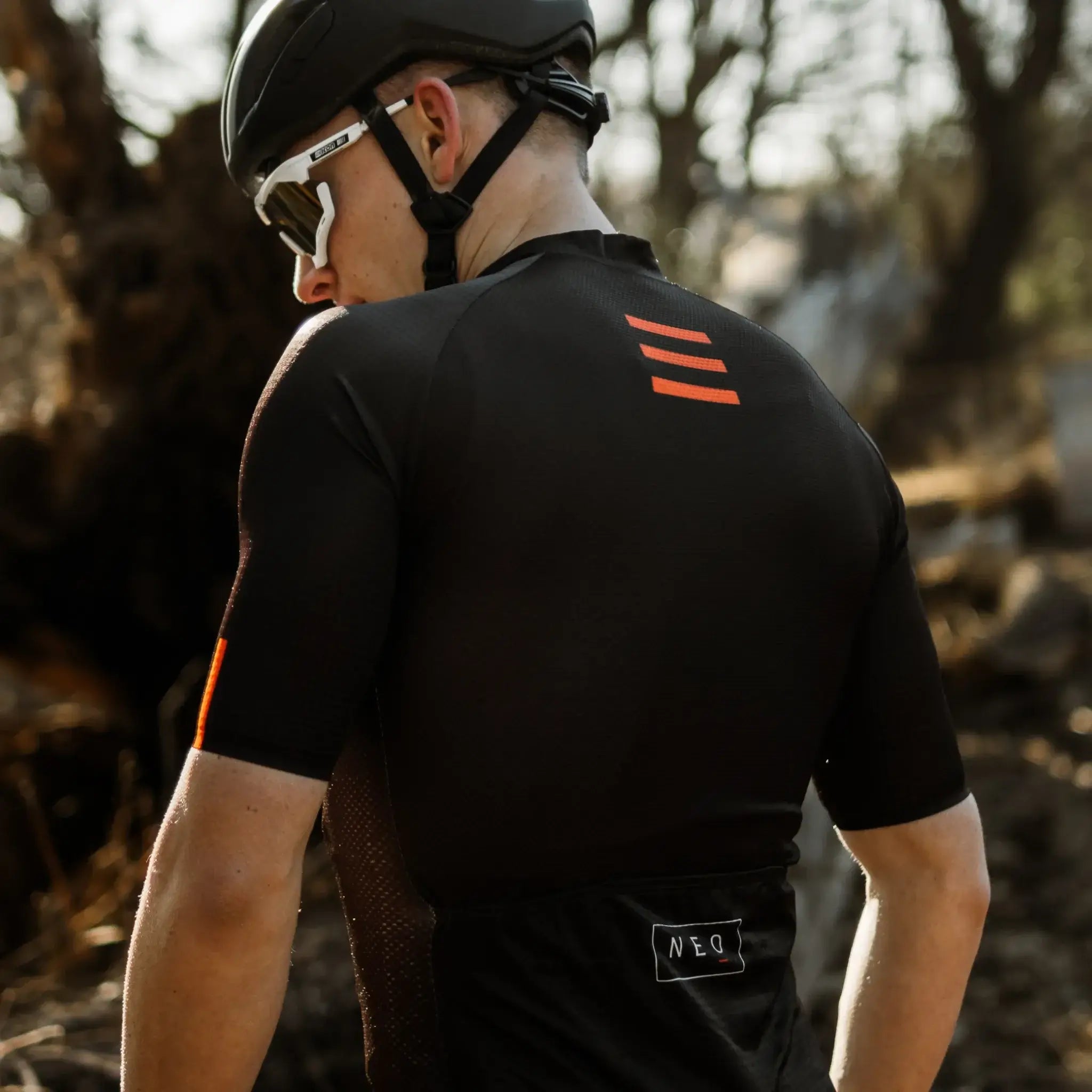 A man posing in a Neo Hyphen Phantom cycling jersey and a helmet, set for a bike ride.