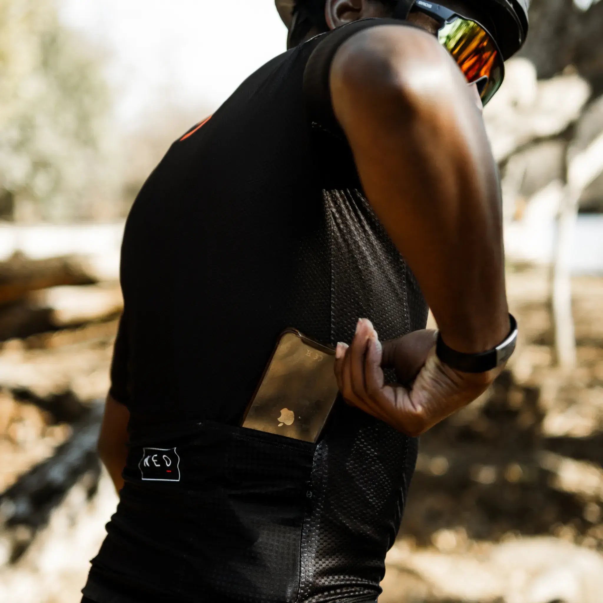 A cyclist wearing a Neo Hyphen Phantom cycling jersey is adjusting the back pocket of his jersey, getting ready for his bike ride.