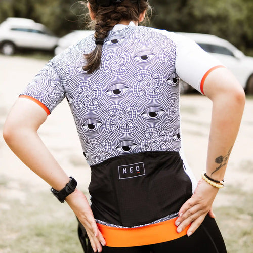 A woman in a stylish black and white Neo Hyphen All-Seeing Eye cycling jersey, enjoying a sunny day outdoors.