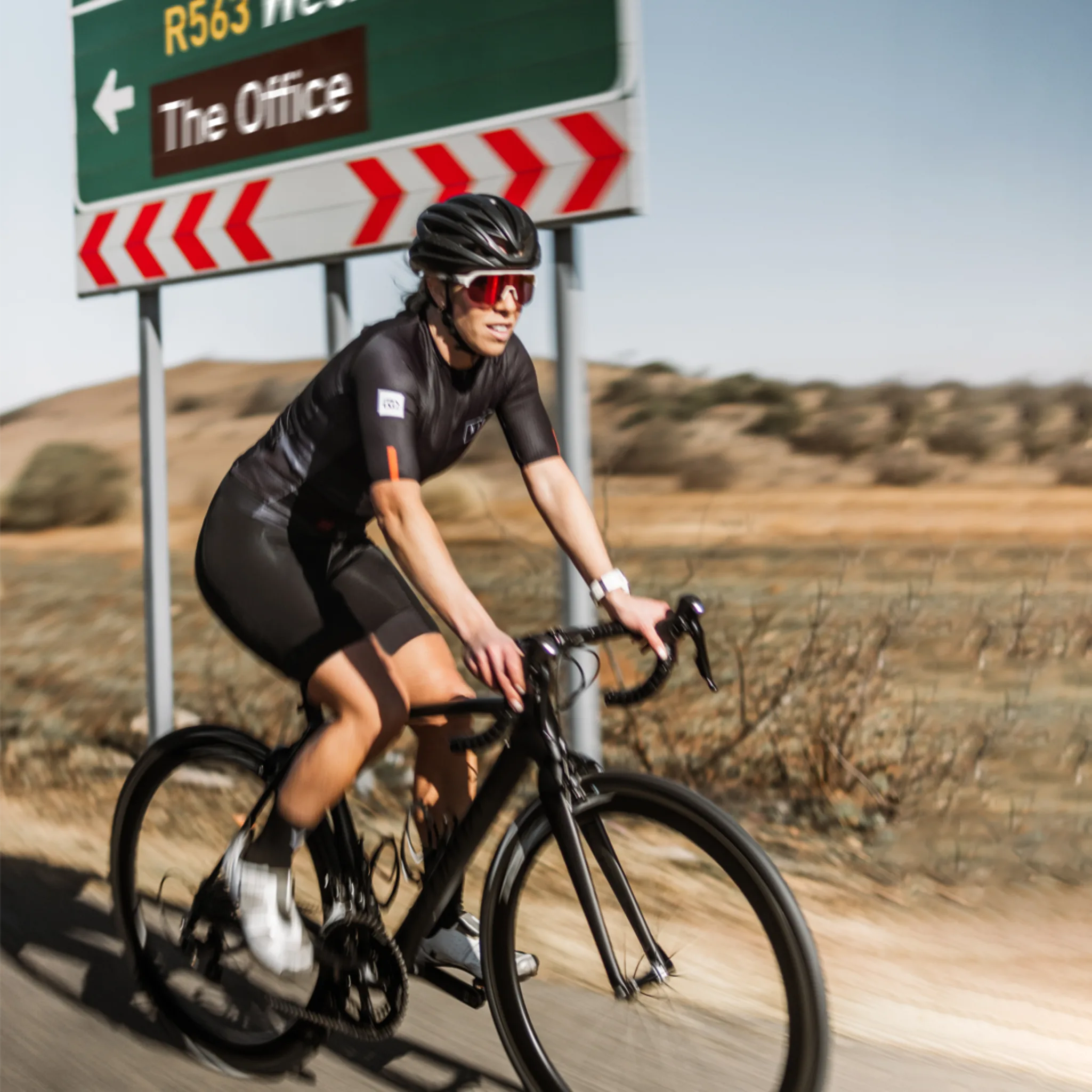 Female cyclist in a Neo Hyphen Phantom cycling jersey sitting on a concrete barrier.